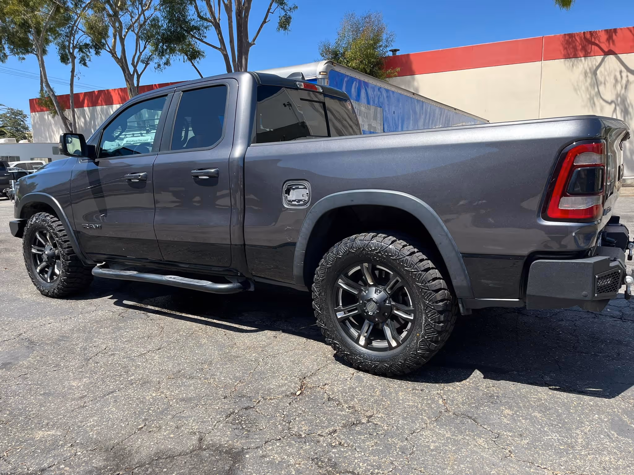 Gray Ram pickup truck parked on cracked pavement under clear blue sky with trees nearby.