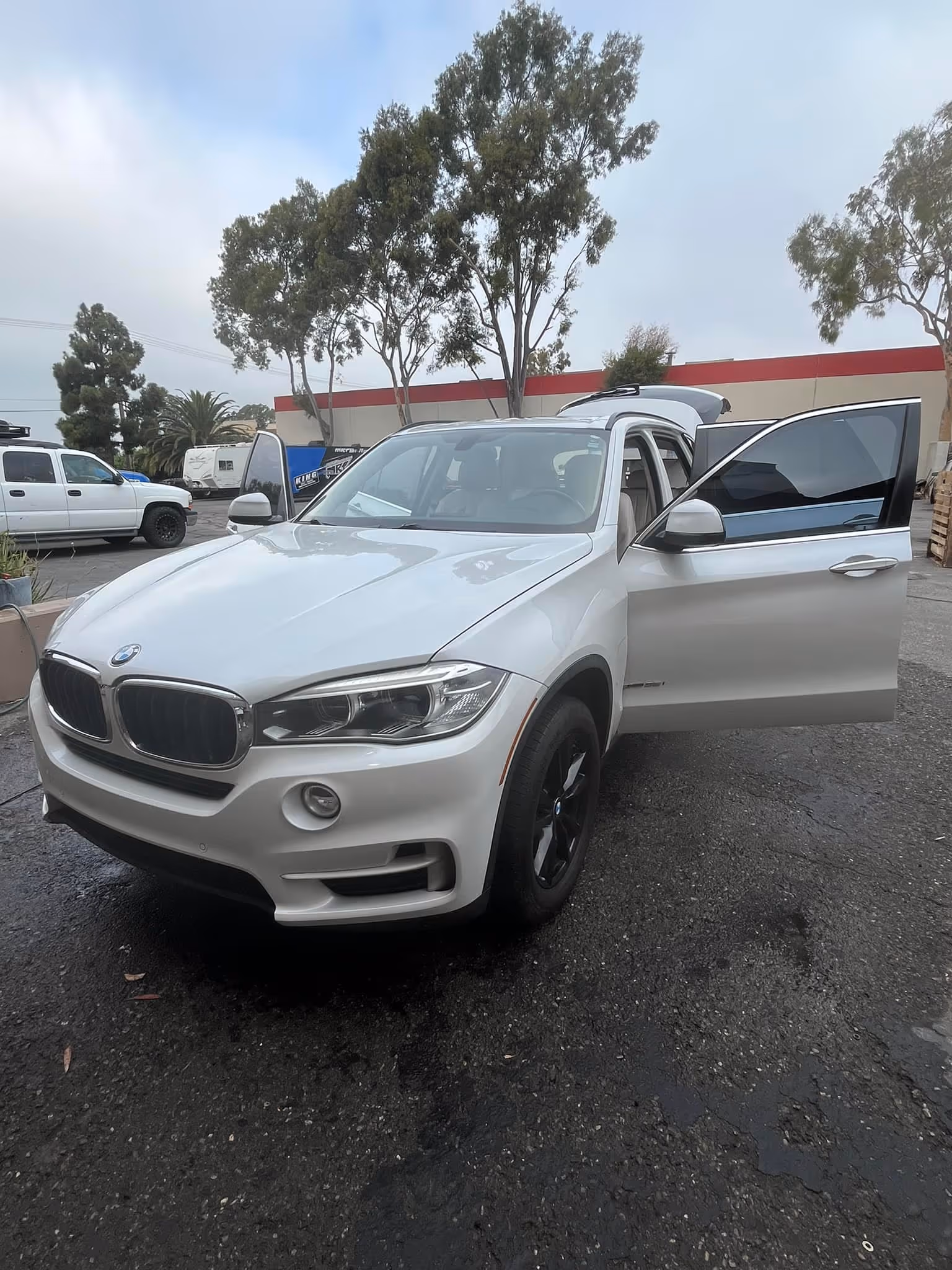 White BMW X5 SUV parked with front and rear passenger doors open in an outdoor lot.
