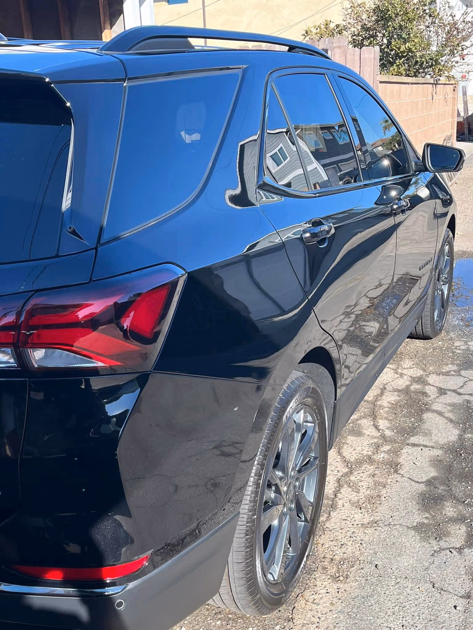 Black SUV parked on cracked pavement with building reflections on windows and body.