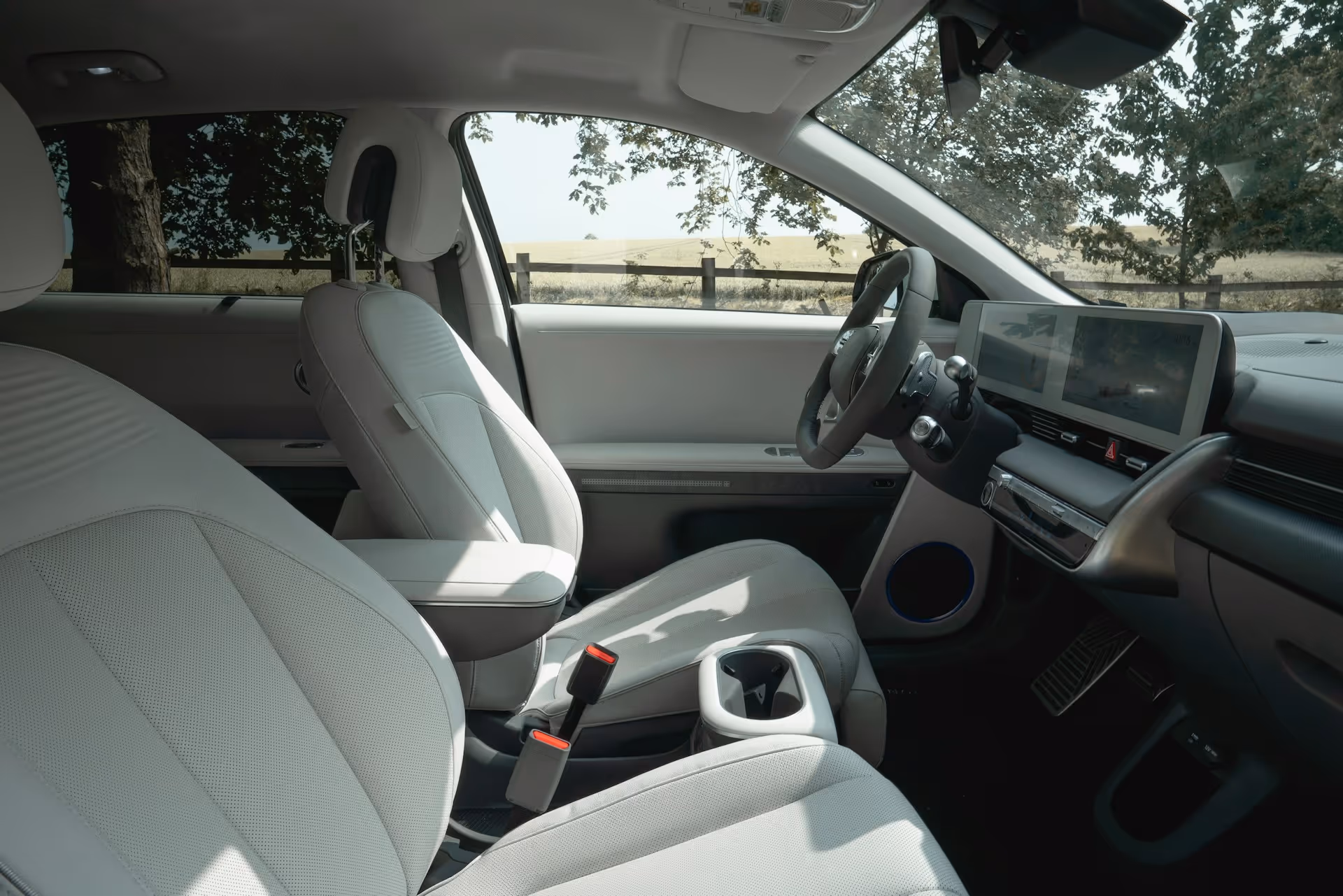 Interior of a modern car with white seats, digital dashboard, and steering wheel with outdoor view.