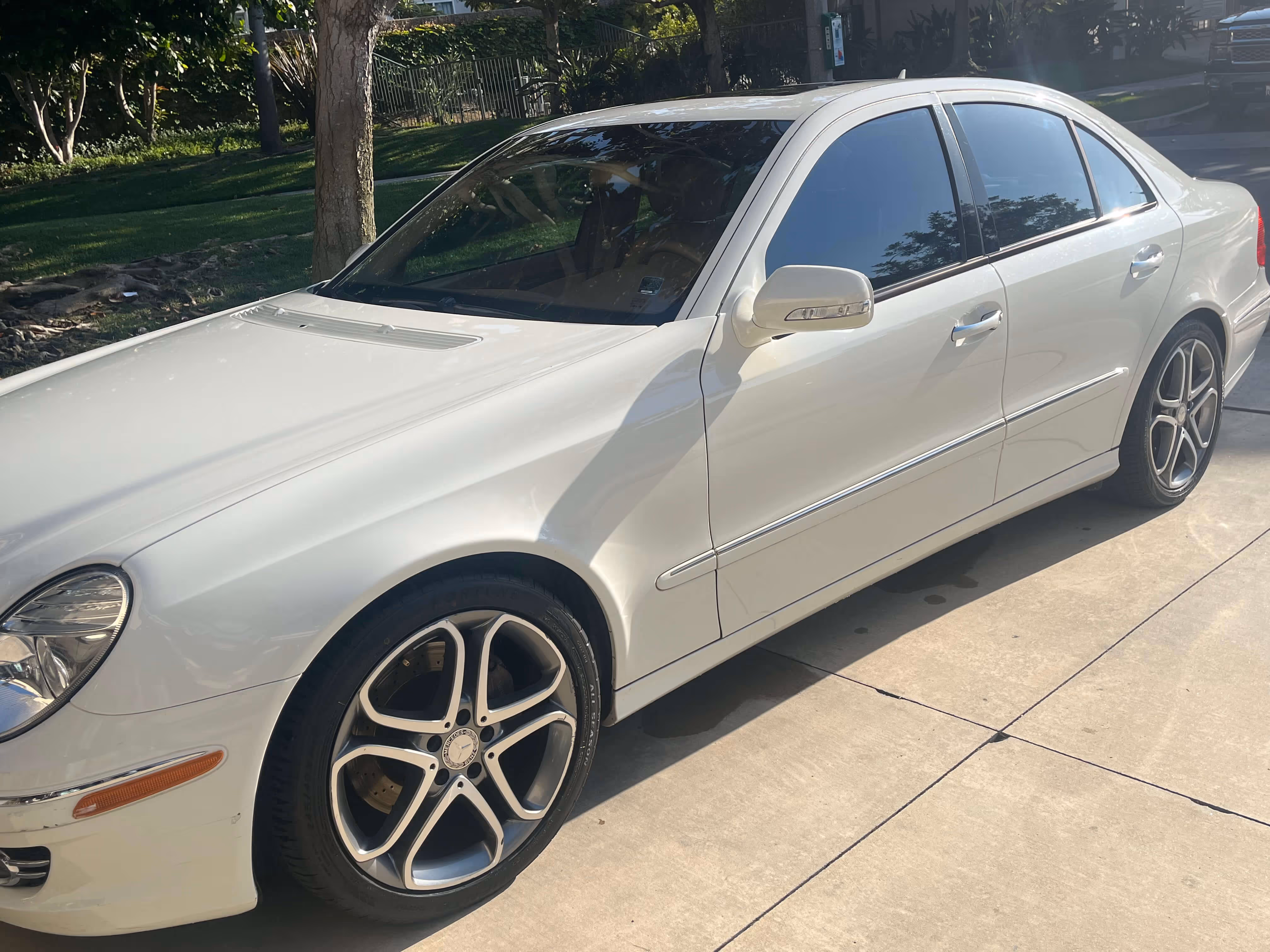 White Mercedes-Benz sedan parked on a concrete surface near grass and trees in daylight.
