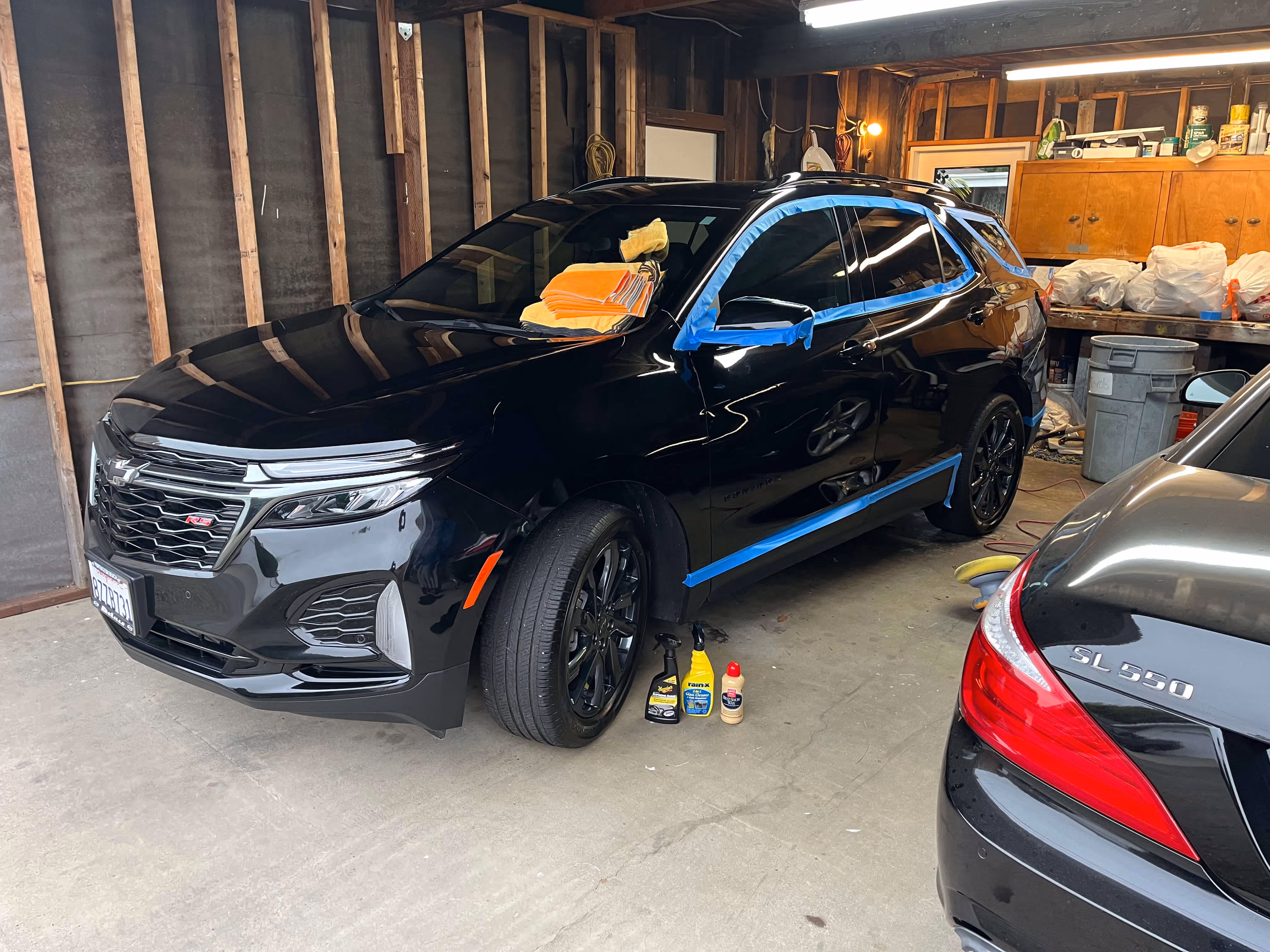 Black Chevrolet SUV being detailed in a garage with cleaning supplies and microfiber towels on it.
